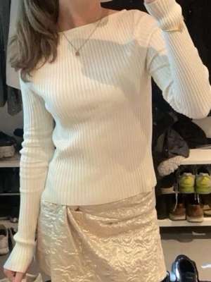 Vit ribbstickad tröja med lång ärm - Säljer en stilren krämvit ribbstickad tröja med lång ärm och rund halsringning. Tröjan har en tight passform och är gjord i ett mjukt, stretchigt material som sitter snyggt på kroppen. Perfekt att matcha med kjol eller jeans.