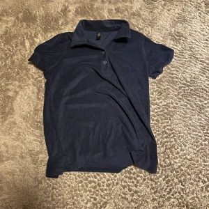 Två kortärmade skjortor i mörka toner - Säljer två skjortor: en mörkblå kortärmad henley med krage och knappdetalj, samt en grå kortärmad skjorta med knappar och två bröstfickor. Båda har avslappnad passform och passar perfekt till vardagslooken.