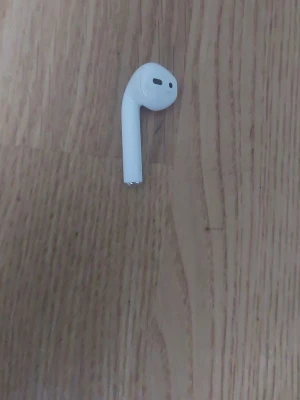 Apple AirPods trådlös hörlur vit - Säljer en vit Apple AirPods hörlur med stilren och minimalistisk design. Hörluren är gjord i blank plast och har den klassiska AirPods-formen som sitter bekvämt i örat. Perfekt för dig som vill ha trådlös frihet och snygg teknik.
