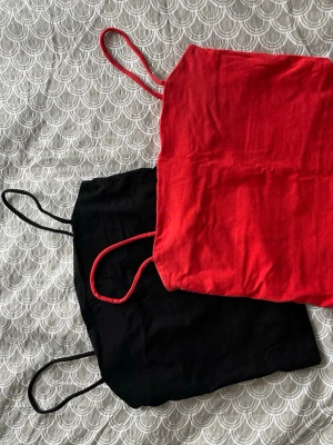 Två linne-toppar i rött och svart - Säljer två stilrena linne-toppar med tunna axelband, en i rött och en i svart. Perfekta att matcha till jeans eller kjol för en enkel och snygg look. Materialet känns mjukt och lätt, perfekt för varma dagar.