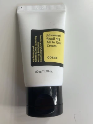 COSRX Advanced Snail 92 Cream - En multifunktionell ansiktskräm från COSRX med snigelsekretfiltrat. Tuben är vit med svart och gul etikett och svart lock. Innehåller 50 g och passar för dig som vill ha återfuktad och mjuk hud. Är använd men finns mycket kvar.