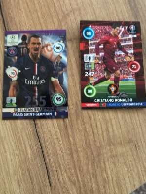 Fotbollssamlarbilder UEFA Euro 2016 - Två samlarkort med fotbollstema, en med PSG-spelare i mörkblå tröja och en med portugisisk spelare i röd matchdräkt. Kortens design har färgstarka detaljer och statistik, perfekta för samlare av fotbollskort.