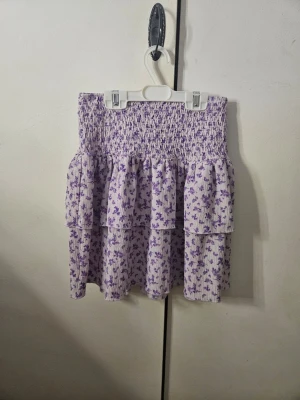 Jättegullig ljuslila blommig volangkjol - Jag säljer en supersöt kort sommarkjol från Gina Tricot i storlek XS. Kjolen är ljuslila med små lila blommor, har smockad midja och volangdetaljer som ger en skön och flowy känsla. Den är en perfekt volangkjol till sommaren, att matcha till söta toppar. Nypris runt 300 kr. I mycket bra skick och använd fåtal gånger. 💓