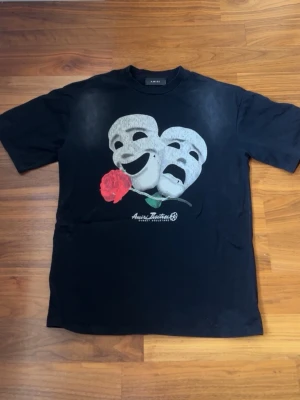 Svart Amitri t-shirt med teatermasker - Cool svart t-shirt från Amiri med tryck av två teatermasker och en röd ros på bröstet. Klassisk passform och rund halsringning. Perfekt för dig som vill sticka ut med en unik och konstnärlig vibe.
