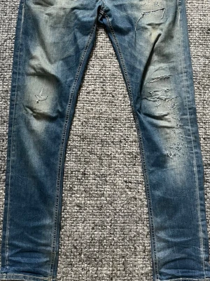 Dondups med slitningar - Säljer ett par blå jeans från Dondup med snygga slitningar och trasiga detaljer på både fram- och baksida. 