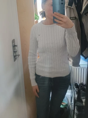 Vit kabelstickad tröja GANT - Säljer en vit kabelstickad tröja från GANT med rund halsringning och långa ärmar. Tröjan har ett diskret GANT-broderi på bröstet och ribbade muddar vid ärmslut och nederkant. Perfekt för en klassisk och stilren look.