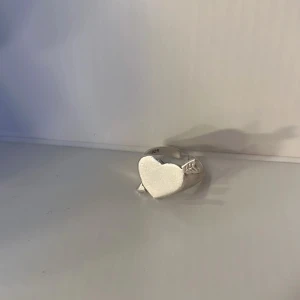Silverring med hjärta och pil - Cool silverring med ett stort hjärta framtill och en pil som går igenom hjärtat. Ringen har en blank finish och är justerbar i storlek. Perfekt för dig som gillar unika smycken med kärlekstema. Använd ett fåtal gånger! Orginal pris cirka 1000kr🥰pris kan diskuteras!