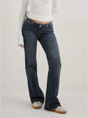 Mörkblå bootcut jeans med låg midja  - Snygga mörkblå bootcut jeans med låg midja och klassiska fem fickor. Jeansen har en lätt tvättad look och råa kanter vid bensluten och i midja. Endast använda en gång, storlek: 32/ short