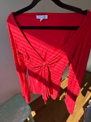 Röd långärmad topp från Design Si - Trendig röd långärmad topp från Design Si med snygg knytning framtill och djup v-ringning. Tunn och mjuk i materialet, perfekt för dig som gillar en lite mer figurnära stil. Passar till både jeans och kjol för en cool look🥂💗