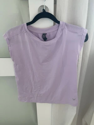 Ljuslila mesh-detaljerad topp - Snygg ljuslila topp från ICANIWILL med mesh-detaljer över axlar och rygg. Toppen är ärmlös och har en avslappnad passform, perfekt för träning eller chill dagar. Tillverkad i mjukt syntetmaterial som andas.