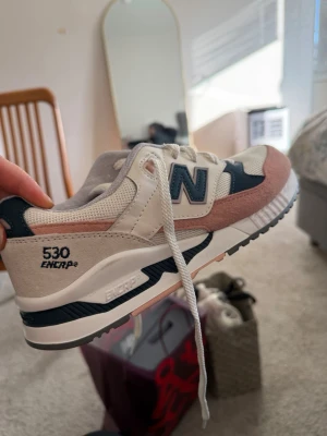 New Balance 530 sneakers beige/blå/rosa - Snygga New Balance 530 sneakers i beige mesh och mocka med detaljer i mörkblått och ljusrosa. Klassisk N-logga på sidan och ENCAP-sula för extra komfort. Perfekta för dig som gillar stilrena och sportiga skor.