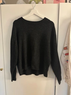 Mörkgrå/svart stickad tröja  - Mysig mörkgrå/svart stickad tröja med rund halsringning och långa ärmar. Perfekt för lager på lager och enkel att matcha med olika stilar. Tröjan har en mjuk och skön känsla, perfekt för kyligare dagar.