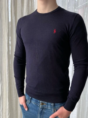 Mörkblå Ralph Lauren merinoull tröja, storlek M - Mörkblå Ralph Lauren sweatshirt med röd logga i 100% merinoull  Bra skick, några små hål som syns vid noga inspektion men annars jättefräsch  Storlek M 