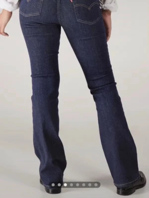 Mörkblå bootcut jeans från Levi's - Snygga mörkblå bootcut jeans från Levi's med klassiska bakfickor och hög midja. Jeansen har en figurnära passform upptill och utsvängda ben. 