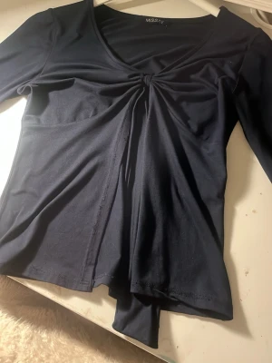 Svart topp med v-ringning från Missay - Trendig svart topp från Missay med v-ringad hals och snygg twistdetalj framtill. Toppen har lång ärm och är tillverkad i ett mjukt, stretchigt material som sitter bekvämt på kroppen. Perfekt att styla med jeans eller kjol.