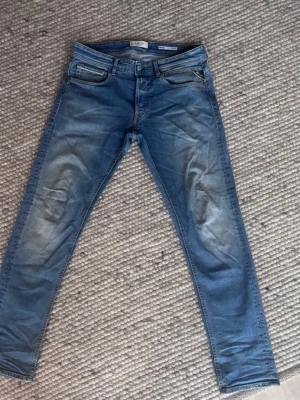 Blå Replay jeans med slitningar - Säljer ett par blå jeans från Replay med snygga slitningar på låren och klassisk femficksmodell. Jeansen har normal midja och raka ben. Tillverkade i bomull med en skön stretch. Perfekta för en avslappnad och trendig look.