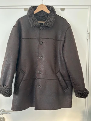 Bastini brun jacka, XL - Klassisk brun vinterjacka / kappa från Bastini i storlek XL.  Högkvalitativt veganskt konstläder och mjukt och varmt teddyfoder och krage. Praktiska fickor på sidorna och dold ficka innanför. En ordentlig kvalitetsjacka. Mycket gott skick.   (Skickas mot porto, men går även att hämta i Stockholm om det är extra bråttom).