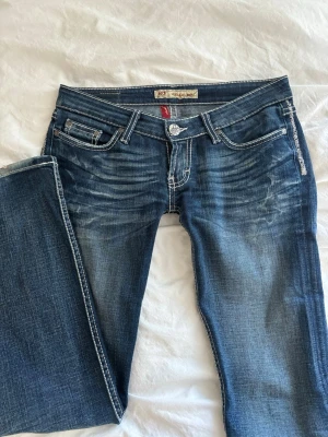 Lågmidjade bootcut jeans  - Säljer ett par blå bootcut jeans. Jeansen har ultra låg midja, klassiska fem fickor och silverfärgade knappar. Märket är BKE Stella boot. Storlek W26/L33. Super snygga men säljer för att dom inte passar mig så bra längre. 