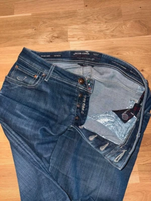 Jacob Cohen blå jeans - Snygga blå jeans från Jacob Cohen med klassisk femficksdesign och raka ben. Jeansen har coola slitningar och detaljerad insida med paisleymönster. Tillverkade i Italien av högkvalitativt denim. Perfekta för dig som gillar stilrena och tidlösa jeans. Nypriset är runt 7000kr.