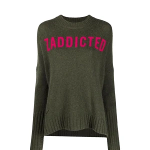 Olivgrön stickad tröja från Zadig & Voltaire - Säljer en olivgrön stickad tröja från Zadig & Voltaire i nyskick med texten 'ZADDICTED' i rosa framtill. Tröjan är tillverkad i 100% merinoull, har långa ärma, ribbade muddar och en något lös passform. Perfekt för dig som gillar statement-plagg. Liten defekt i handen (bild 5), men inget stort!💗