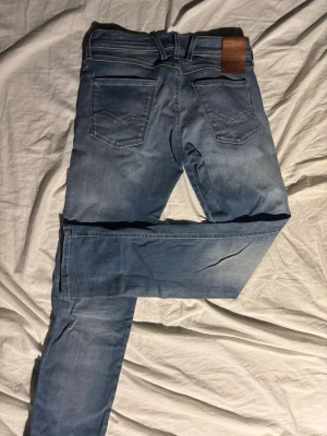 Replay Anbass blå jeans - Snygga blå Replay Anbass jeans med klassisk femficksdesign och läderpatch bak i midjan. Jeansen har en slim passform och är tillverkade i mjukt jeansmaterial med lätt tvättad look. Perfekta för dig som gillar stilrena och moderna jeans. W29 L32