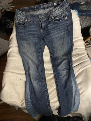 Blå Miss Me jeans med broderade fickor - Säljer ett par blå Miss Me jeans med snygg slitning och broderade bakfickor med detaljer i vitt och silver. Klassisk femficksmodell med låg midja och raka ben. Jeansen är i denim och har coola metalldetaljer på fickorna. Omsydda från skinny till flare (inte av mig) men sitter bra som vanliga flare. Ca 80-85cm mellan ände och skrev