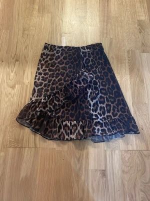 Leopardmönstrad volangkjol. - Snygg kjol med leopardmönster i bruna och svarta toner. Kjolen har volangdetaljer längs nederkanten och omlottkänsla framtill. Tillverkad i ett lätt och något transparent material som ger ett flowy intryck. Perfekt för dig som vill sticka ut med ett djurmönster.