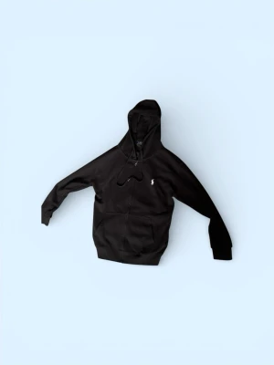 Svart hoodie från Polo Ralph Lauren - Klassisk svart hoodie från Polo Ralph Lauren med huva och dragsko. Har en liten vit logga broderad på bröstet och en stor magficka framtill. Tillverkad i mjukt bomullsmaterial och har ribbade muddar vid ärmar och nederkant.