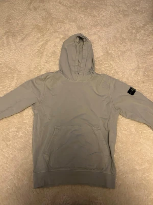 Ljusgrön Hoodie från Stone Island  - Säljer en ljusgrå hoodie från Stone Island med klassisk huva och känguruficka framtill. Tröjan har en svart stone island logga på vänster ärm och är gjord i mjukt bomullsmaterial. Perfekt för en avslappnad och stilren look.hör av er vid funderingar 😁😁🔥🔥