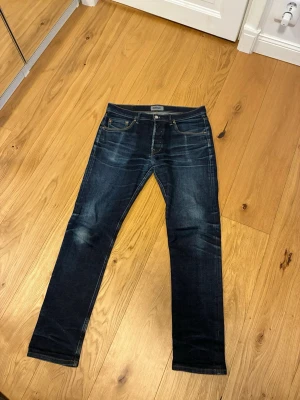 Mörkblå jeans från WESC - Säljer ett par mörkblå jeans från WESC med helt sjuka fades och galet snygga slitningar framtill. Jeansen har raka ben och kontrastsömmar som ger en schysst look. Perfekta för dig som gillar en avslappnad men stilren stil. 