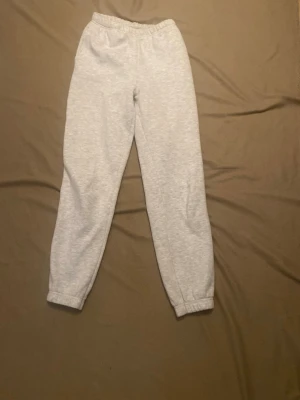 Grå mjukisbyxor med resår - Snygga ljusgrå mjukisbyxor med resår i midjan och vid bensluten. Klassisk rak passform och superbekväma för chill dagar. Tillverkade i mjukt sweatshirtmaterial som känns skönt mot huden. Perfekta för en avslappnad stil.