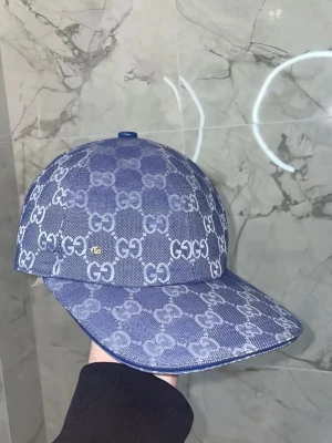 Blå GG-monogram keps från Gucci - Säljer en blå keps från Zara med det klassiska GG-monogrammet i vitt över hela kepsen. Kepsen har böjd skärm och är tillverkad i ett slitstarkt tygmaterial. Perfekt för dig som vill ha en stilren och lyxig accessoar med tydlig logga.