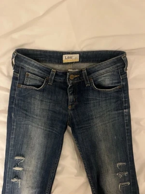 Lågmidjade Lee jeans - Supersnygga Lee jeans med hål och slitningar. Låg midja med bootcut. Fint skick. De är i Lee’s ungdoms storlek men de passar mig som är 163 och brukar ha XS. Innerbenslängd: 71 cm Midja: 34 cm rakt över. Kan skicka fler bilder!