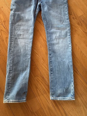 Levi's 501 ljusblå raka jeans - Säljer ett par klassiska ljusblå jeans från Levi's med rak passform och fem fickor. Jeansen har den ikoniska röda Levi's-lappen på bakfickan och läderpatch i midjan. Perfekta för en avslappnad och tidlös stil.