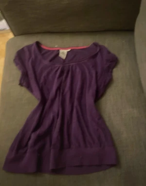 Lila topp med kort ärm - Snygg lila topp med korta ärmar och rund halsringning. Modellen är lite lösare och har en bredare mudd nertill. Perfekt att styla med jeans eller kjol för en chill look.