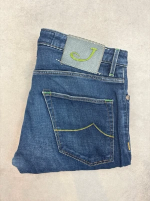 Blå jeans från Jacob Cohen - Snygga blå jeans från Jacob Cohen med raka ben och klassisk femficksdesign. Jeansen har gröna detaljer på bakfickan och ett grått patch med grön J-logga i midjan. Tillverkade i mjuk denim med gul kontrastsöm för en cool look.