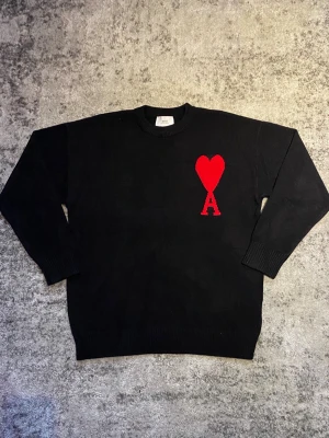 Svart Ami Paris tröja - Riktigt fet Ami tröja i svart med röd logga på bröstet. Tröjan är storlek S och skicket är mycket bra, utan  några defekter. Perfekt för dig som söker en stilren look med en gnutta elegans. Hör gärna av dig om funderingar som mått, pris, bilder etc. Så löser vi! 😁