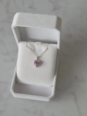 Halsband med lila hjärthänge - Sött halsband med ett hjärtformat lila hänge i glittrande stenar.