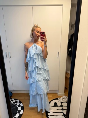 Ljusblå volangklänning med halterneck - Supersöt långklänning i ljusblått med flera lager volanger och halterneck. Klänningen är ärmlös och har en flowy, romantisk look som passar perfekt till sommaren. Materialet känns lätt och luftigt.