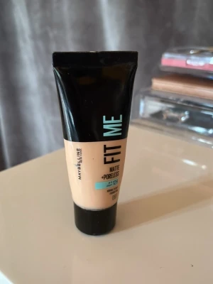 Maybelline Fit Me Matte + Poreless foundation - Maybelline Fit Me Matte + Poreless foundation i nyansen 100. Kommer i en smidig tub på 30 ml. Ger en matt finish och jämnar ut hudtonen, perfekt för normal till oljig hy. Tuben är svart och beige med turkosa detaljer. (Inte full med mycket kvar!)💓🌸