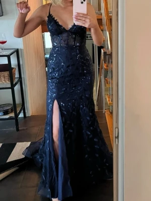 Marinblå balklänning med slits - Elegant marinblå balklänning med smala axelband, transparent överdel och v-ringning. Klänningen har glittriga detaljer, slits framtill och figurnära passform. Perfekt för bal eller festligare tillställningar!🥰😍