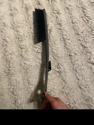 Isskrapa med borste i plast och metall - Praktisk isskrapa med svart borste och grått handtag i plast. Skrapdelen är i metall och har ett trekantigt grepp. Perfekt för att ta bort is och snö från bilen under vintern.