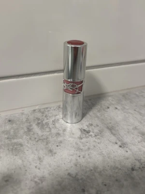 YSL  läppstift loveshine 122 - Lyxigt läppstift från Yves Saint Laurent i en elegant silvrig hylsa med dekorativ YSL-detalj. Färgen är en mjuk rosa nyans som ger en fräsch look. Perfekt för dig som vill ha ett stilrent och exklusivt läppstift i sminkväskan. Den är enbart testad på handen.