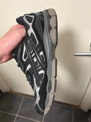 Svarta Asics NYC-Gel sneakers - Snygga svarta Asics Gel-Sonoma sneakers med mesh och syntetpaneler. Skorna har en chunky sula och klassisk snörning. Perfekt för dig som gillar sportig och stilren look. Diskreta detaljer och bekväm passform.