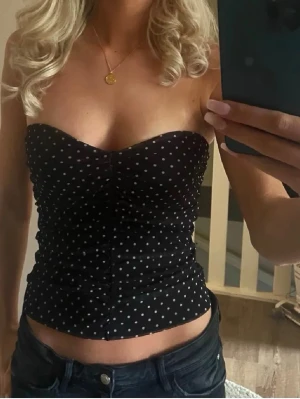 Svart prickig tubtopp Bikbok - Svart tubtopp med vita prickar och rynkade detaljer framtill. Toppen är axelbandslös och har en tight passform som framhäver figuren. Perfekt för en trendig och ungdomlig stil.