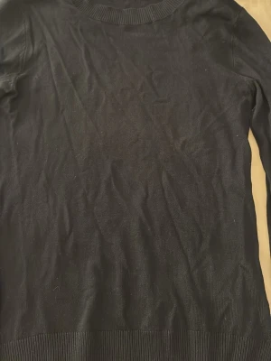 Svart stickad tröja från 157 - En svart, klassisk stickad tröja från 157 med rund halsringning och ribbade muddar vid hals, ärmslut och nederkant. Enkel och stilren design som passar till det mesta. Perfekt basplagg i garderoben.