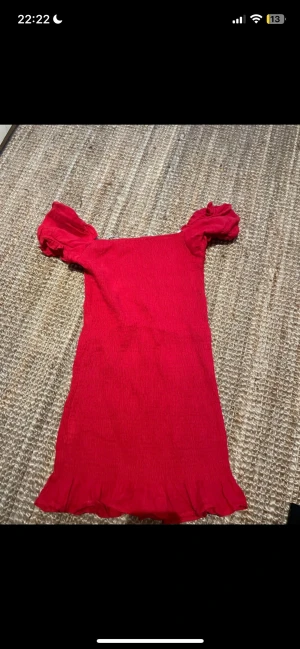Röd kort puffärmad klänning - Säljer en röd kort klänning med puffärmar och volangkant nertill. Klänningen har en smickrande, kroppsnära passform och är tillverkad i ett stretchigt tyg som känns bekvämt. Perfekt för dig som vill ha en enkel men snygg look.