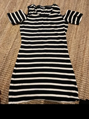 Randig kortklänning från ONLY - Snygg svartvit randig kortklänning från ONLY med offshoulder-ärmar. Klänningen har en figurnära passform och är tillverkad i mjuk bomull. Perfekt för dig som gillar en enkel men trendig stil.