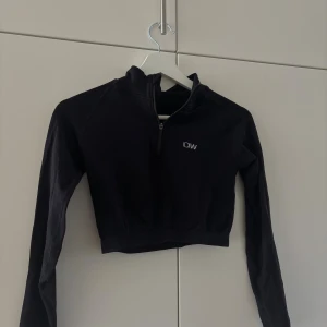 Svart cropped ziptröja från ICANIWILL - Svart långärmad cropped ziptröja från ICANIWILL med halv dragkedja framtill och diskret logga på bröstet. Tillverkad i ett stretchigt funktionsmaterial som passar perfekt till träning eller som ett sportigt lager. Passar nog även S