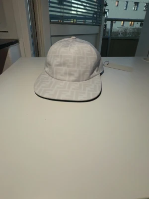 Vit F keps med FF-mönster - Säljer en stilren vit keps från F med det klassiska FF-monogrammet ton-i-ton över hela kepsen. Kepsen har böjd skärm och justerbar passform. Perfekt accessoar för dig som gillar exklusiva detaljer och italiensk design.